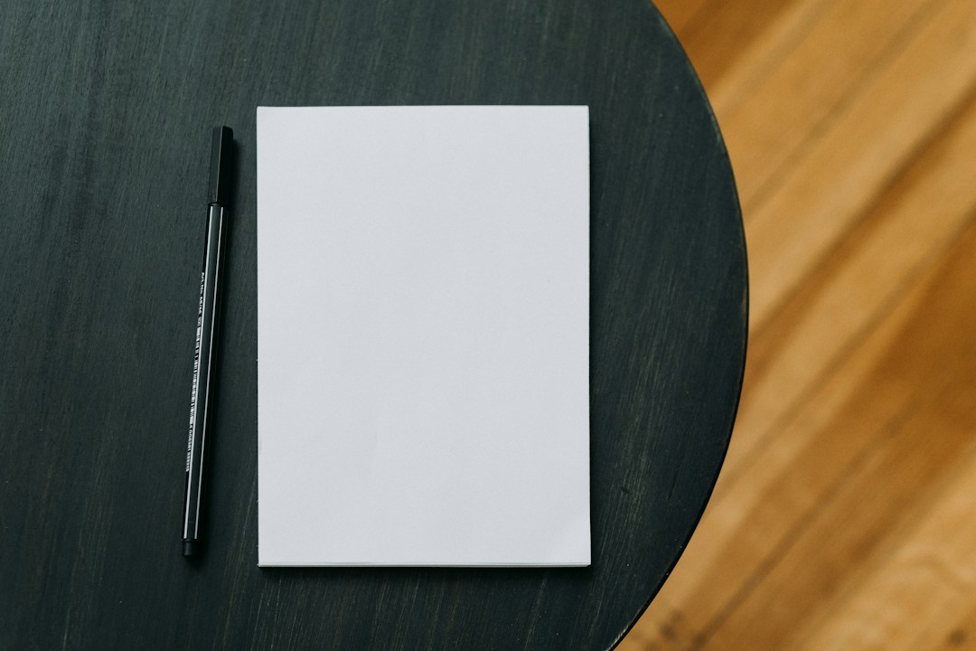 Blank white notepad and black pen on a dark table